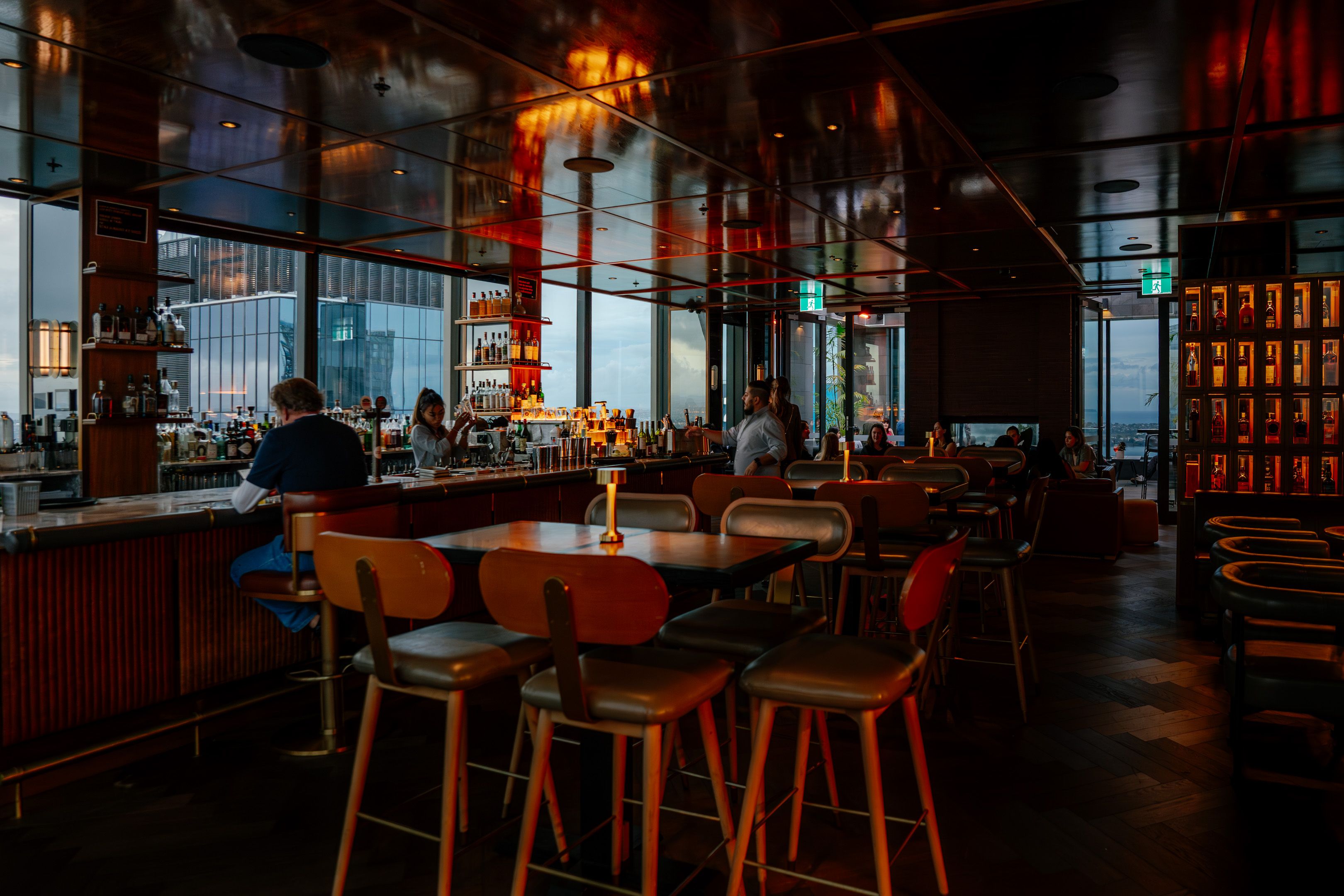 Guests enjoying drinks in a warmly lit rooftop bar with city skyline views.