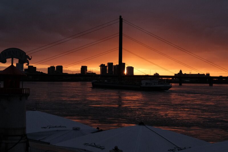 Sunset over the Rhine in Düsseldorf, with a bridge and the city skyline silhouetted in the evening light.
